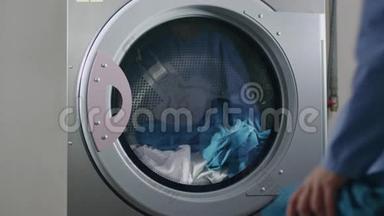 女士在工业洗衣机里装制服。 工业洗涤衣